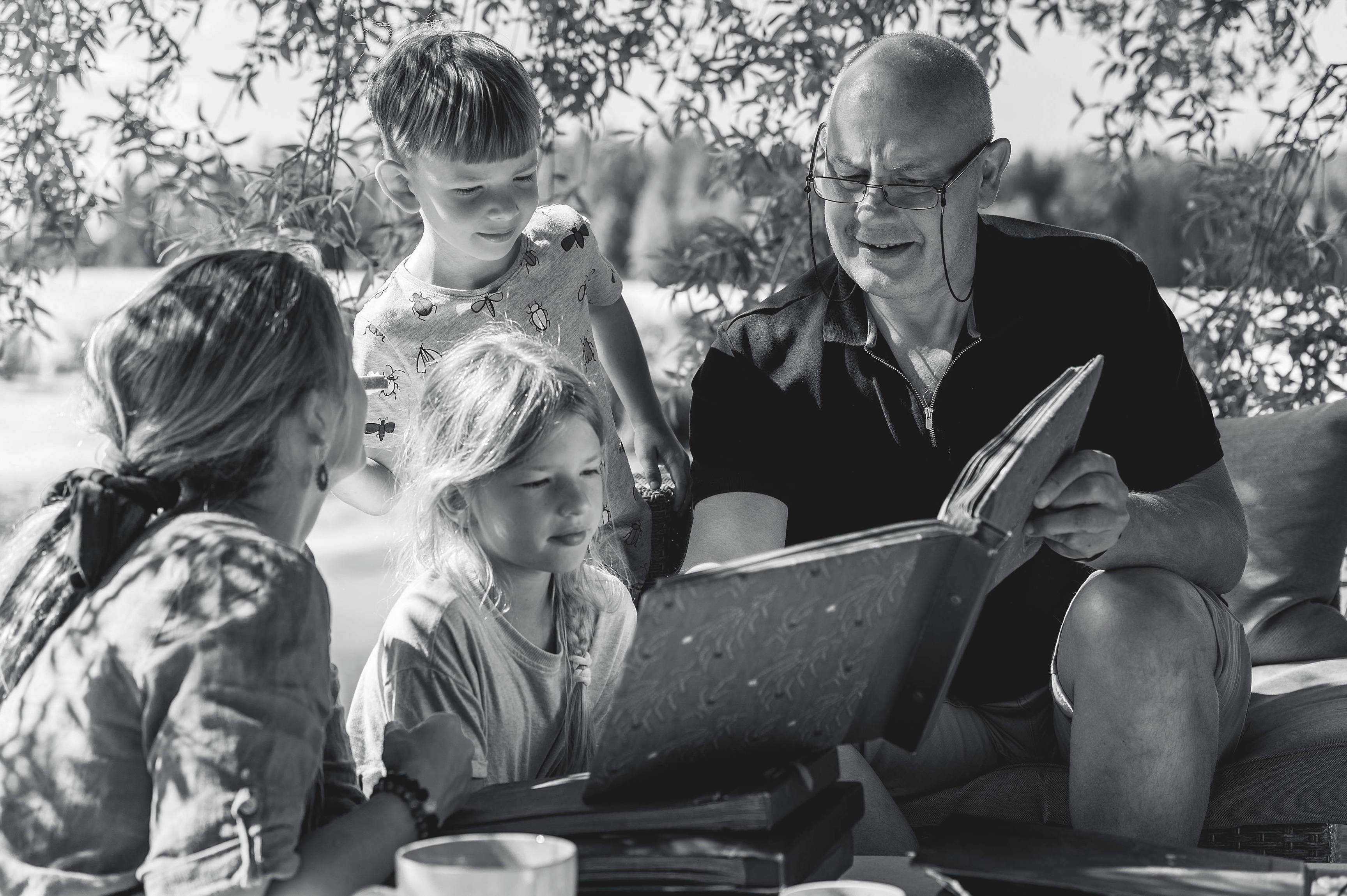 Grandpa with his grandchildren looking at old photo albums on outdoor terrace on a sunny summer day