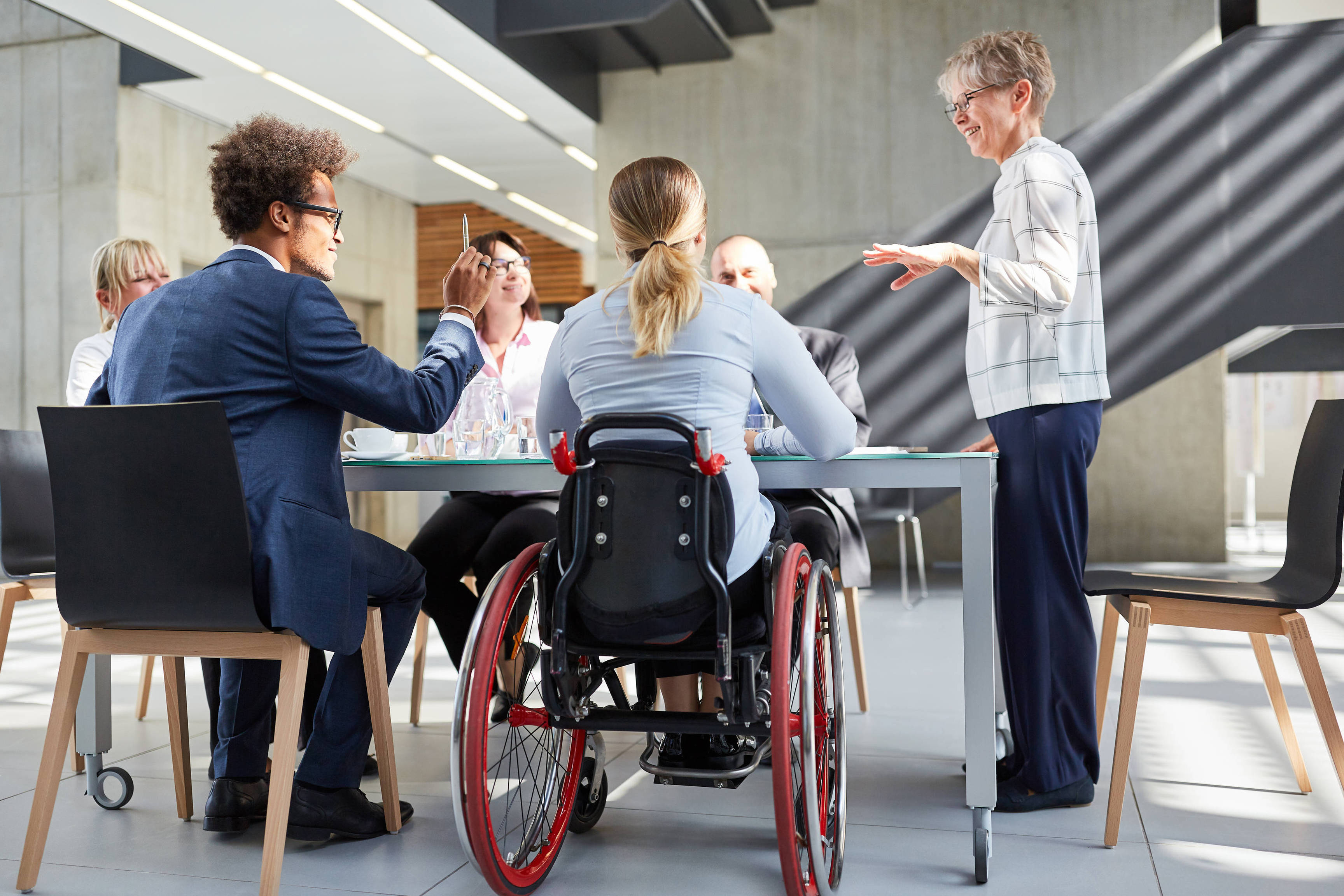 Gruppe Geschäftsleute in einem Meeting mit Kollegin im Rollstuhl für Inklusion